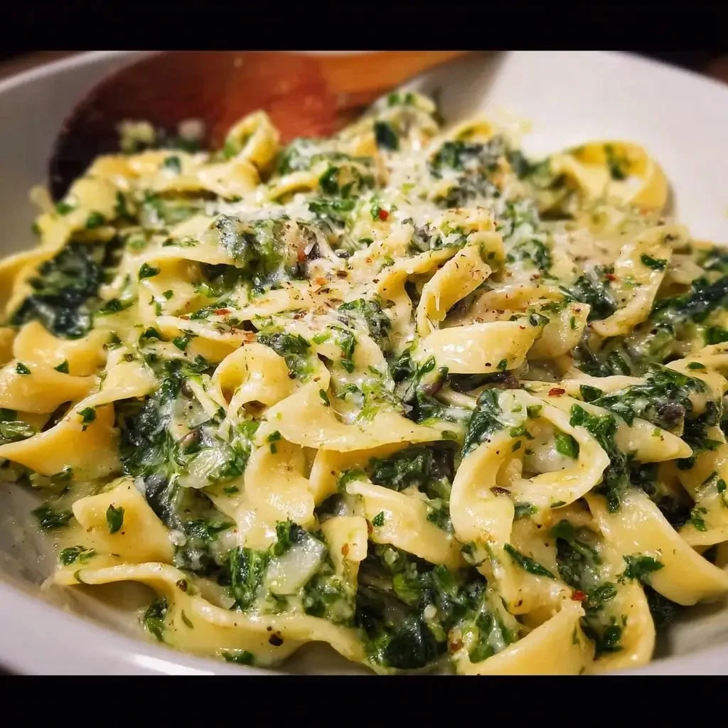 A bowl of creamy garlic spinach pasta garnished with fresh spinach and cheese