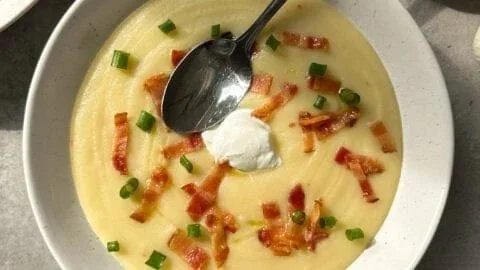 Bowl of creamy potato leek soup garnished with fresh herbs and bread