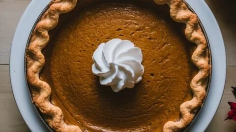 Delicious homemade pumpkin pie with whipped cream on a wooden table