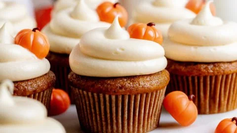 Pumpkin cupcakes topped with brown sugar cream cheese frosting on a rustic table.