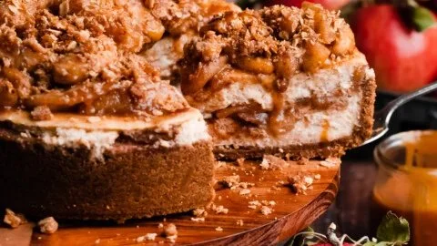 Slice of salted caramel apple pie cheesecake topped with caramel drizzle and apple slices.